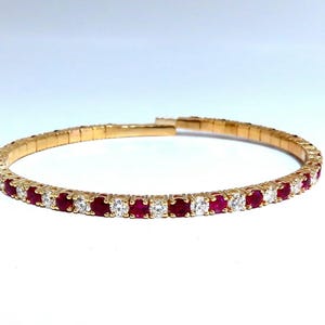May include: A flexible gold-tone stretch bracelet featuring an alternating pattern of round, faceted deep red rubies and clear, sparkling white stones set in a continuous row. The band is constructed with expandable metal links for a comfortable fit.