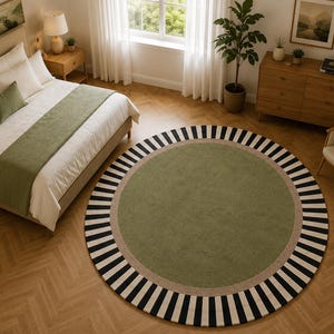 May include: A large circular area rug featuring a solid sage green center, a thin beige border, and an outer edge with alternating black and white vertical stripes. The rug is positioned on a light brown herringbone wood floor in a bedroom.