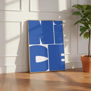 Könnte beinhalten: Ein rechteckiger Wandkunstdruck in einem dünnen goldenen Rahmen mit dem Wort NICE in großen, fetten, blauen serifenlosen Großbuchstaben auf weißem Hintergrund. Die Buchstaben sind in einem Zwei-mal-zwei-Raster innerhalb des Rahmens angeordnet.