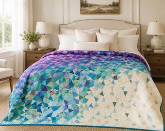 Könnte beinhalten: Eine Steppdecke mit einem geometrischen Muster aus kleinen Dreiecken in einem Farbverlauf, der von Dunkelviolett und Blau auf der linken Seite zu hellem Türkis und Weiß auf der rechten Seite übergeht. Die Decke liegt auf einem Bett mit weißen Kissen.