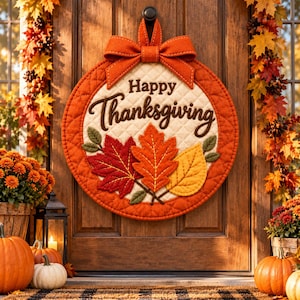 May include: A round, quilted fabric door sign featuring the text Happy Thanksgiving in dark brown script. The sign is decorated with three felt autumn leaves in red, orange, and yellow, and is topped with a large, orange fabric bow.