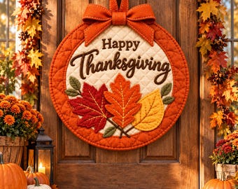 Könnte beinhalten: Ein rundes, gestepptes Türschild aus Stoff mit dem Schriftzug Happy Thanksgiving in dunkelbrauner Schreibschrift. Das Schild ist mit drei Filzblättern in Rot, Orange und Gelb verziert und mit einer großen, orangen Stoffschleife versehen.