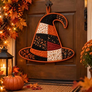May include: A quilted fabric witch hat wall hanging featuring a patchwork design of black, orange, and cream fabrics with floral, leaf, and crescent moon patterns. The hat has a curved top and a wide brim, finished with orange fabric binding.