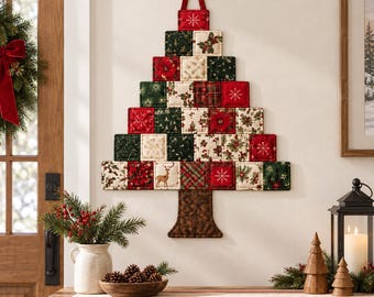 Könnte beinhalten: Eine Wanddekoration in Form eines Weihnachtsbaums aus gesteppten Stoffquadraten in Rot, Grün und Creme. Die Quadrate zeigen Muster mit Weihnachtssternen, Stechpalmen, Schneeflocken und einem Hirsch. Ein brauner Stoffstamm ist an der Basis befestigt.
