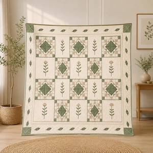Puede incluir: Una colcha cuadrada con un patrón repetitivo de bloques alternos. Algunos bloques muestran un diamante verde central rodeado por una cuadrícula beige y blanca, mientras que otros presentan un tallo vertical con hojas y una flor en tonos verdes y beige.