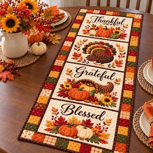 May include: A rectangular quilted table runner featuring three distinct panels with autumn themes. The panels display pumpkins, a turkey, and a cornucopia, accompanied by the words Thankful, Grateful, and Blessed in a dark brown script font.