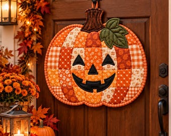 Könnte beinhalten: Ein gesteppter Wandbehang aus Stoff in Kürbisform mit einem Patchwork-Design aus orangefarbenen, braunen und cremefarbenen Stoffen mit verschiedenen Mustern. Der Kürbis hat ein schwarzes, aufgesticktes Jack-o'-Lantern-Gesicht, einen braunen Stiel und ein grünes Blatt.