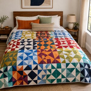 Puede incluir: Una colcha de patchwork con un patrón geométrico de triángulos en varios colores, incluyendo naranja, azul, rojo, verde y amarillo. La colcha está extendida sobre una cama con almohadas blancas, un cojín lumbar naranja y uno a rayas.