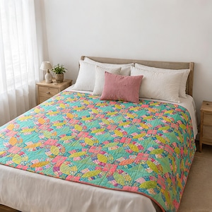 Könnte beinhalten: Eine Steppdecke mit einem sich wiederholenden Muster aus ineinandergreifenden Ringen in leuchtenden Türkis-, Limettengrün-, Pink- und Orangetönen. Die Decke liegt auf einem Bett mit weißen Kissen und einem einfarbigen pinken Kissen.