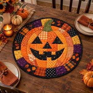 May include: A round quilted placemat featuring a central jack-o'-lantern design constructed from various orange, black, and yellow fabric patches. The pumpkin has a green stem and a black face, surrounded by a border of assorted autumn-themed patterns.