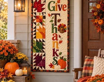 Könnte beinhalten: Ein vertikaler, gesteppter Wandbehang mit dem Schriftzug Give Thanks in bunten Buchstaben, verziert mit herbstlichen Stoffblättern, einem Truthahn und Kürbissen. Die linke Seite zeigt eine Spalte aus Patchwork-Blättern in Rot, Orange, Gelb und Grün.