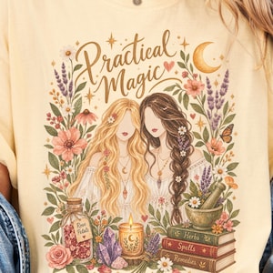 May include: A butter yellow t-shirt featuring a graphic print with the text Practical Magic. The design includes two figures surrounded by flowers, a crescent moon, a jar labeled Rose Petals, a candle, crystals, and a stack of books labeled Herbs, Spells, and Remedies.