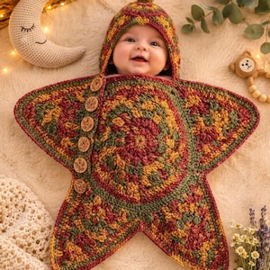 May include: A star-shaped crochet baby bunting in variegated shades of burgundy, mustard yellow, and forest green. The hood features a small acorn topper, and the side is fastened with five round wooden buttons engraved with floral designs.