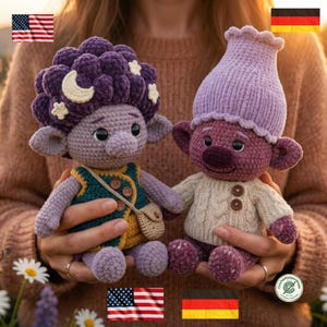 May include: Two handmade crochet dolls with plush textures. The left doll has dark purple hair with a cream moon and stars, wearing a teal vest and tan satchel. The right doll wears a light purple hat and a cream-colored cable knit sweater.