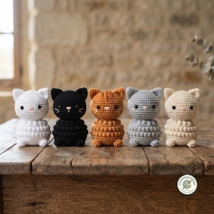 May include: Five small, handmade crochet cat figurines arranged in a row. The cats are white, black, orange, grey, and cream, each featuring round black eyes, a small stitched nose, and a textured, rounded body with a distinct bobble stitch pattern.