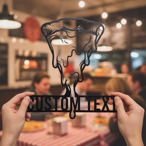 Könnte beinhalten: Ein schwarzes Metallschild mit einem stilisierten Pizzastück, bei dem Käse nach unten tropft, und dem Schriftzug CUSTOM TEXT in fetten Großbuchstaben am unteren Rand, gestaltet als dekoratives Element.
