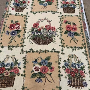Peut inclure: Un plaid tissé présentant un motif en grille de panneaux rectangulaires alternés. Le design affiche des compositions florales dans des paniers et des bouquets de fleurs dans des tons de rouge, bleu et blanc, encadrés par des bordures de lierre vert.