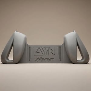May include: A matte gray plastic controller grip accessory featuring two ergonomic handles on the sides and a central bridge section. The center panel displays the embossed text AYN and the word thor in a stylized lowercase font with vertical lines.