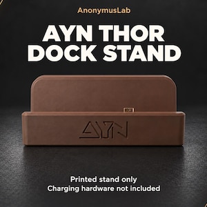 May include: A brown Ayn Thor dock stand featuring the text AnonymusLab, AYN THOR DOCK STAND, AYN, and Printed stand only Charging hardware not included. The rectangular dock stand has a central slot and a smooth, matte finish.