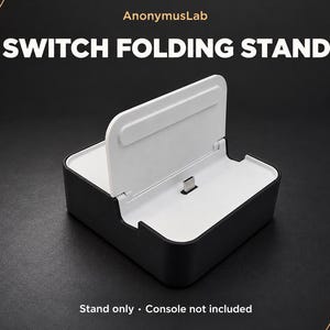 May include: A black and white folding stand for a gaming console, featuring the text AnonymusLab, SWITCH FOLDING STAND, and Stand only · Console not included. The device has a central USB-C connector and a hinged back support panel.