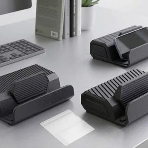 May include: Three black rectangular phone stands with a ribbed, textured surface design. Each stand features a wide base and a raised, angled support ledge to hold a mobile device in a horizontal position. The stands are made of a matte material.