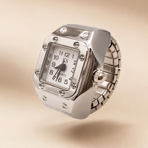 Puede incluir: Un anillo reloj de tono plateado con esfera cuadrada, fondo blanco, números arábigos negros y el texto KS y QUARTZ. El bisel presenta ocho tornillos decorativos y la banda consiste en un diseño de eslabones metálicos extensibles.