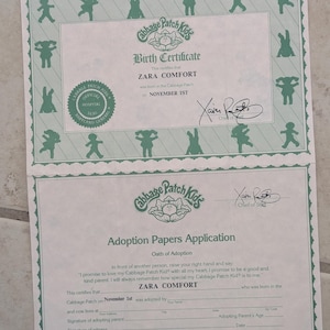 May include: A Cabbage Patch Kids birth certificate and adoption papers application for Zara Comfort. The documents are printed in green ink on white paper, featuring the Cabbage Patch Kids logo, an official hospital seal, and a signature.