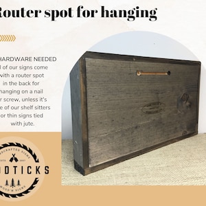 May include: The back of a wooden sign with a router spot for hanging. The sign is brown and has a white label with the text "HANDCRAFTED SIGNS ESTD 2007 WOODTICKS WOOD'N SIGNS".
