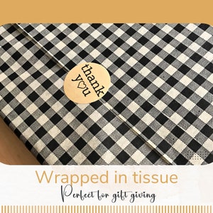 Puede incluir: Un regalo envuelto en papel de seda a cuadros blancos y negros, sellado con una pegatina redonda que dice "thank you" con un coraz&oacute;n. El texto "Wrapped in tissue" y "Perfect for gift giving" est&aacute; debajo.