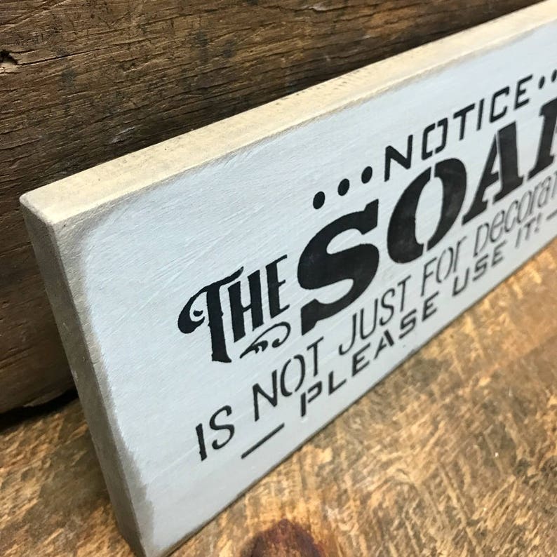 May include: A white wooden sign with black lettering that reads "...NOTICE... THE SOAP IS NOT JUST FOR DECOR - PLEASE USE IT!"