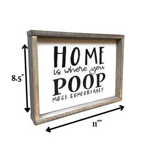 Puede incluir: Un letrero rectangular de madera con fondo blanco y marco gris. El letrero dice "HOME is where you POOP MOST COMFORTABLY" en letras negras. El letrero mide 28 cm de ancho y 22 cm de alto.