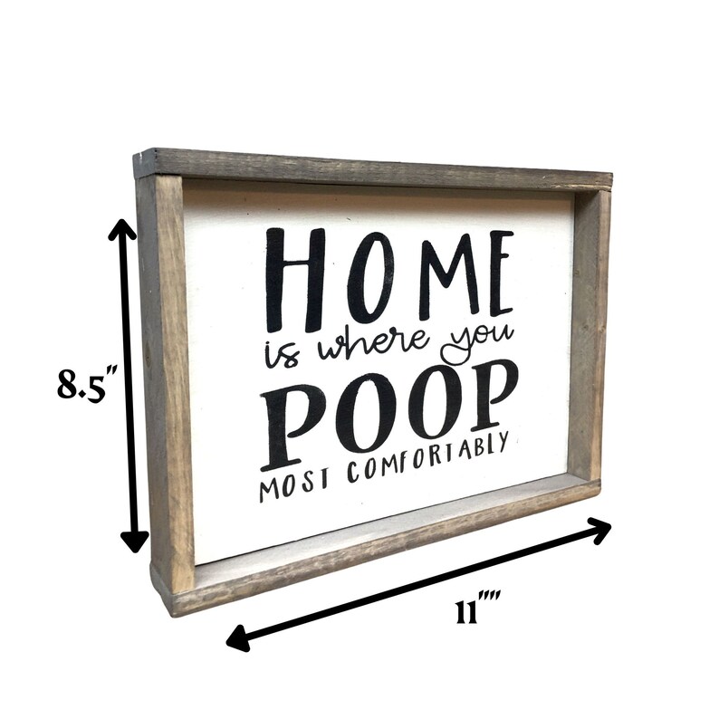 Puede incluir: Un letrero rectangular de madera con fondo blanco y marco gris. El letrero dice "HOME is where you POOP MOST COMFORTABLY" en letras negras. El letrero mide 28 cm de ancho y 22 cm de alto.