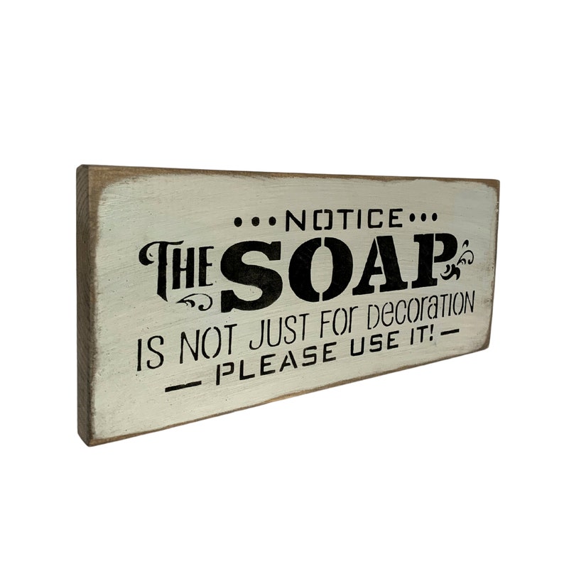 May include: A white wooden sign with black lettering that reads "...NOTICE... THE SOAP IS NOT JUST FOR DECORATION PLEASE USE IT! - "