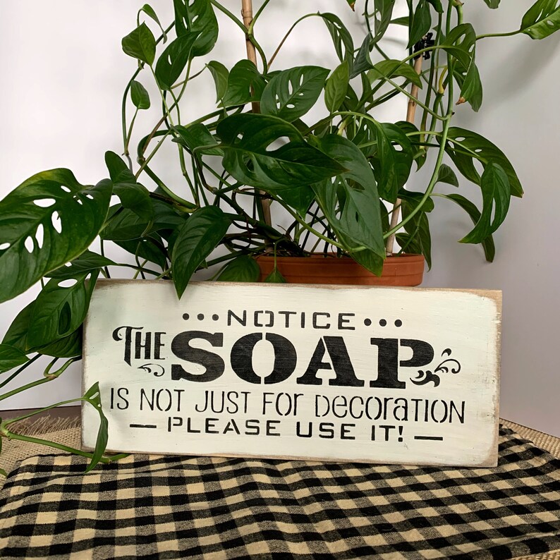 May include: White wooden sign with black text that reads "NOTICE... THE SOAP IS NOT JUST FOR DECORATION - PLEASE USE IT! - "