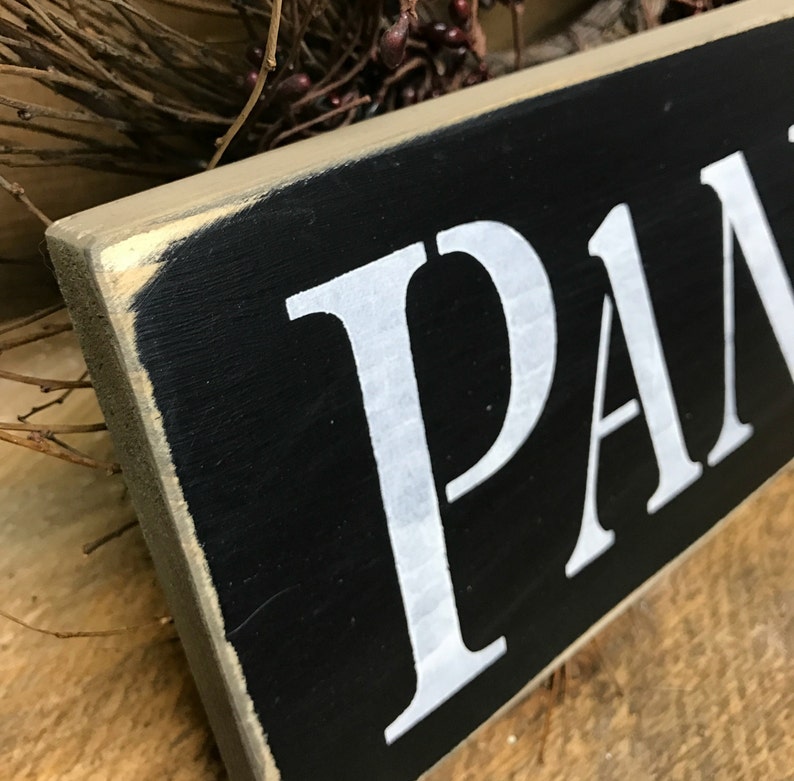 May include: A black wooden sign with white painted letters spelling "PANTRY". The sign has a distressed, rustic look.