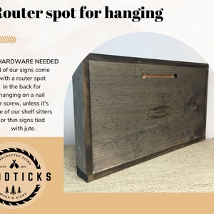 Puede incluir: Un letrero de madera con un punto de enrutador para colgar. La parte posterior del letrero es visible, mostrando un acabado gris oscuro y un agujero precortado para colgar. El texto dice "Punto de enrutador para colgar" y "No se necesita hardware."