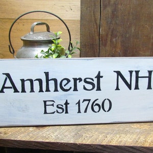 May include: White wooden sign with black text that reads "Amherst NH Est 1760".
