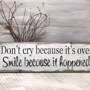May include: A white wooden sign with black lettering that reads "Don't cry because it's over Smile because it happened".