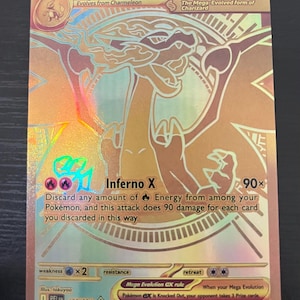 May include: A gold-colored Mega Charizard X EX trading card with a holographic finish. The card features a stylized illustration of the dragon-like creature, 360 HP, the Inferno X attack text, and the Mega Evolution EX rule printed at the bottom.