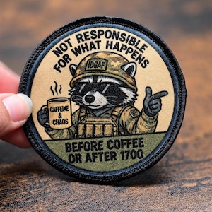 Peut inclure: Un écusson brodé circulaire représentant un raton laveur portant un casque camouflage avec le texte IDGAF, des lunettes de soleil et un équipement tactique. Il tient une tasse marquée CAFFEINE & CHAOS. Le texte indique NOT RESPONSIBLE FOR WHAT HAPPENS BEFORE COFFEE OR AFTER 1700.