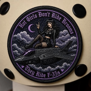 Puede incluir: Un parche bordado circular que muestra una figura de cabello oscuro con ropa negra sentada sobre un avión de combate F-35 contra un cielo nocturno estrellado y nublado con una luna creciente. El texto dice: Hot Girls Don't Ride Brooms, They Ride F-35s.