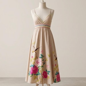 May include: A beige midi dress with thin spaghetti straps and a V-neckline. The waist features a horizontal striped band in pastel colors. The skirt is decorated with an embroidered pattern of large pink and white flowers and small birds.