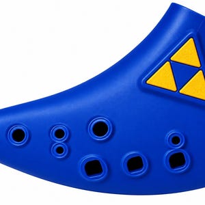 May include: A blue ocarina wind instrument featuring a yellow triangular triforce emblem on its upper surface. The instrument has a curved, elongated shape with multiple circular and square finger holes arranged along the front for playing music.