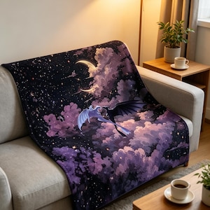 May include: A rectangular throw blanket featuring a dark night sky filled with stars, a crescent moon, and purple clouds. Two dragon-like creatures, one light blue and one black, are depicted flying together against the celestial background.