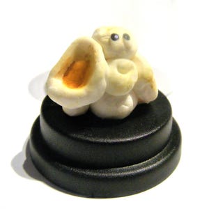 May include: A white popcorn sculpture with a brown spot on one of the pieces. The sculpture is sitting on a black circular base.