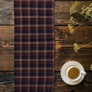 May include: A rectangular table runner featuring a plaid pattern in shades of dark navy blue, deep burgundy, and thin white lines. The fabric is positioned vertically, displaying a consistent grid design across its entire visible surface area.