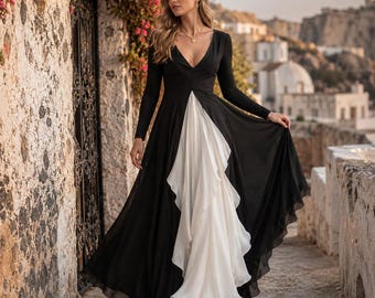 May include: A floor-length dress featuring a black bodice with long sleeves and a deep V-neckline, contrasted by a flowing white pleated skirt panel at the center. The garment has a fitted waist and a flared silhouette that reaches the ground.