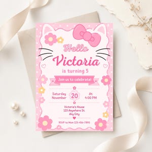 A pink cat-themed birthday invitation with a large pink bow, cat ears, and whiskers, lying on a white envelope with a pink ribbon and pearls.