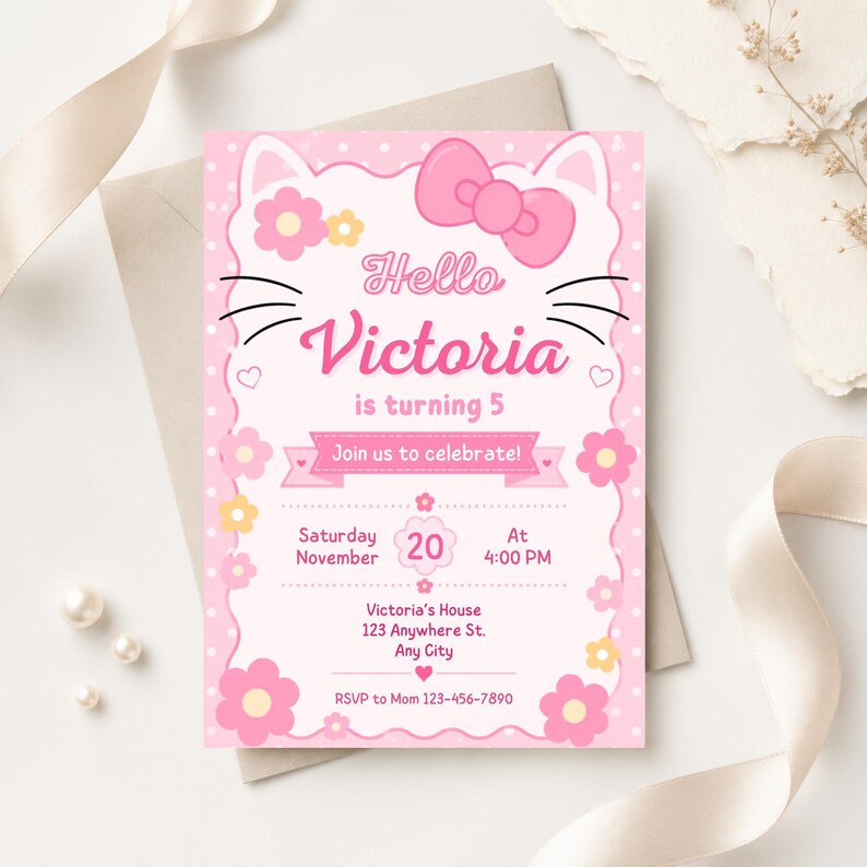 A pink cat-themed birthday invitation with a large pink bow, cat ears, and whiskers, lying on a white envelope with a pink ribbon and pearls.