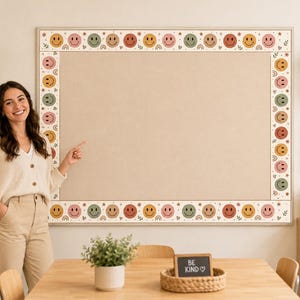 Puede incluir: Un tablón de anuncios rectangular con un borde decorativo que presenta un patrón repetitivo de caras sonrientes coloridas, pequeños arcoíris, estrellas y hojas. El tablón tiene una superficie de corcho lisa de color beige claro.